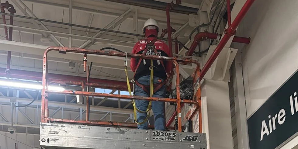 Técnico de MET ONE trabajando en altura sobre plataforma tijera en la bodega de un centro de distribución